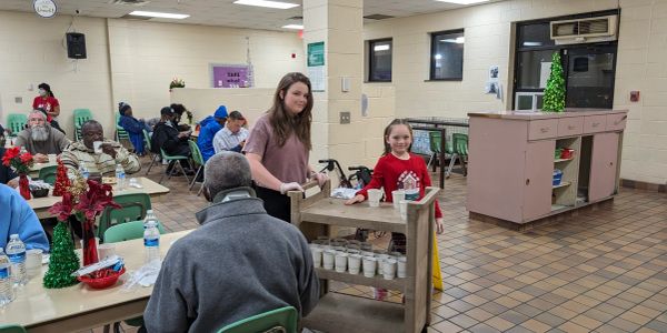 Volunteers serve drinks to elderly people in a community center during a holiday event.