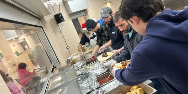 Volunteers serving food in a community kitchen line.