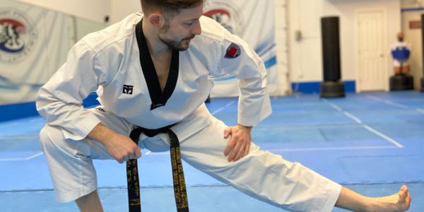 Man in martial arts uniform stretching on dojo mat.