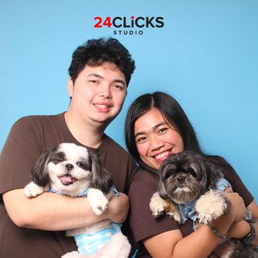 Happy couple posing with two small dogs against a blue backdrop.