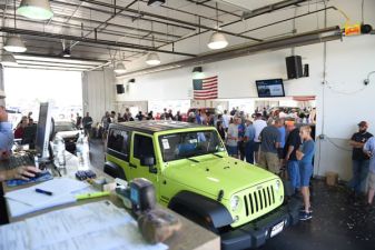 A bright green Jeep inside a busy auction house with people gathered.