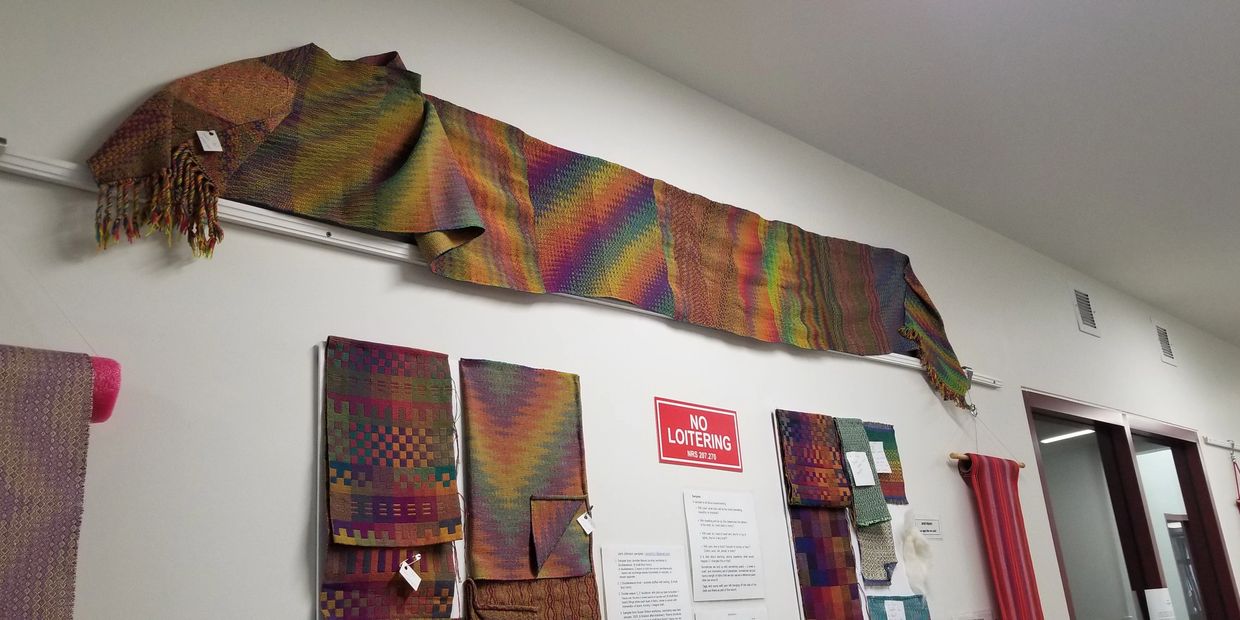 Colorful woven textiles displayed on a wall in an exhibition setting.