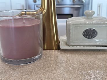 Purple candle, brass decor, and ceramic butter dish on kitchen counter.