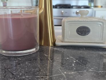 A pink candle, brass vase, and white butter dish on kitchen counter.