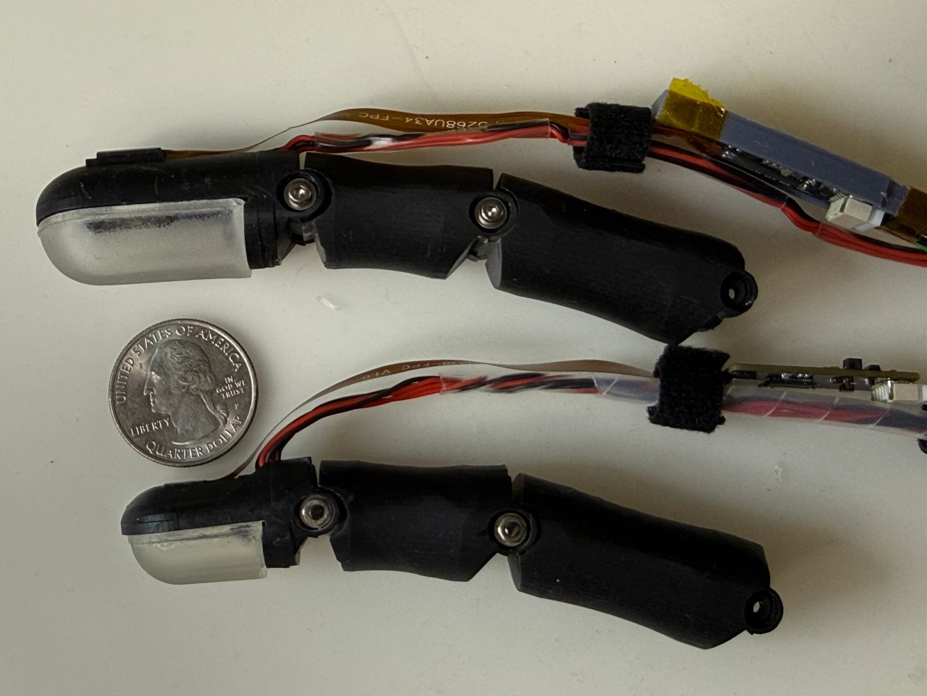 Two prototype humanoid robotic fingers with optical tactile sensors, shown with a U.S. quarter.