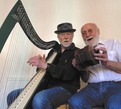 Two elderly men playing harp and accordion, smiling and engaged.