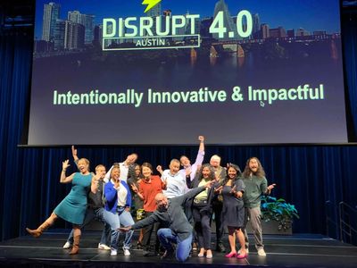 Group of people joyfully posing on stage at Disrupt 4.0 Austin event.