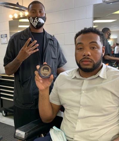 Two men in a barbershop, one holding hair product.