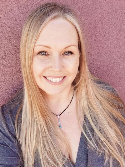 Smiling woman with long blonde hair against a pink wall.