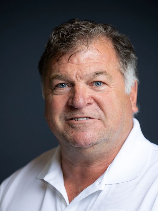 Portrait of a middle-aged man with blue eyes wearing a white polo shirt.