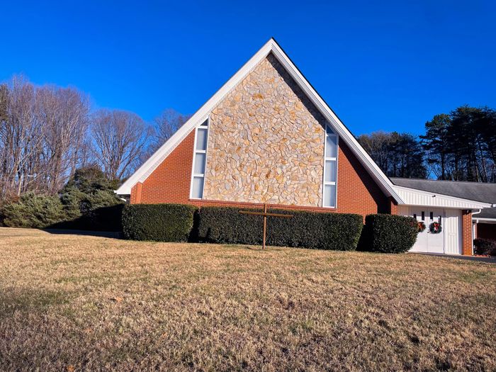 A brick church with a stone facade and Christmas wreaths on the doors under a clear blue sky.