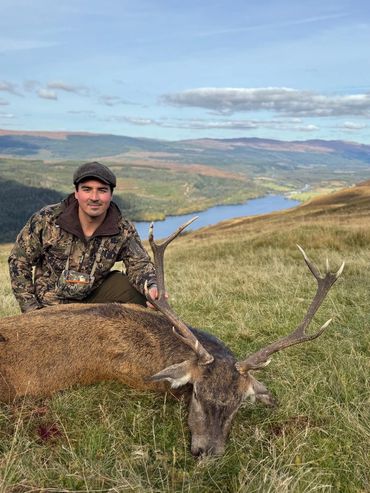 Hunter posing with a deer on a hillside overlooking a river valley.