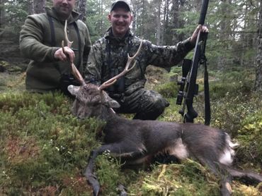 Two hunters posing with a deer they hunted in the forest.