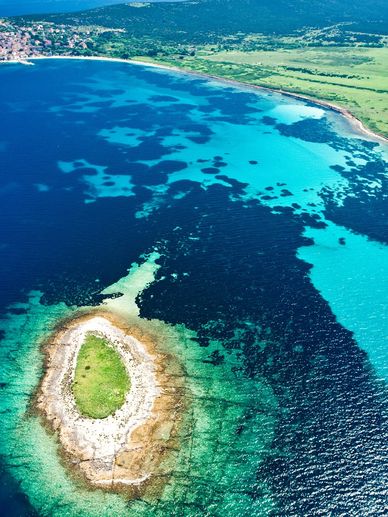 Aerial view of a small island near the coast with vibrant blue waters.