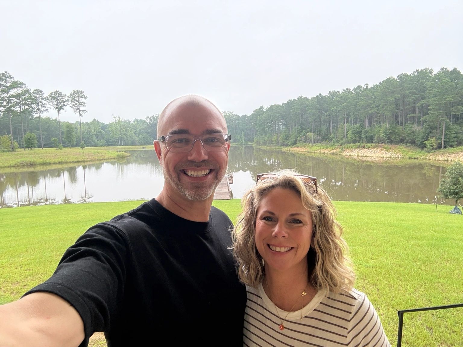 Smiling couple posing by a serene lake and forest.