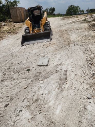 A yellow skid steer loader on a dirt construction site under a clear sky.