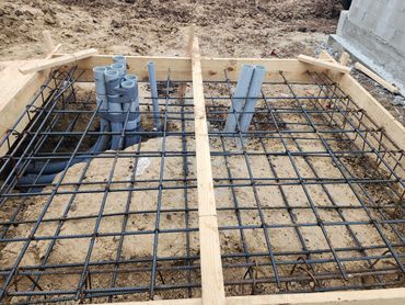 Construction site showing rebar grid and embedded pipes in wooden frame.