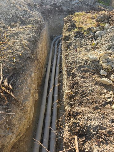Three gray pipes installed in a narrow trench on a construction site.