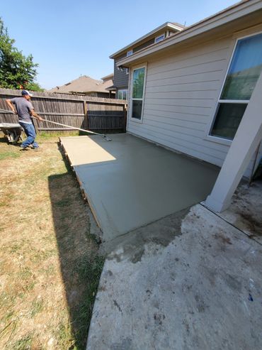 A man smooths freshly poured concrete next to a house.