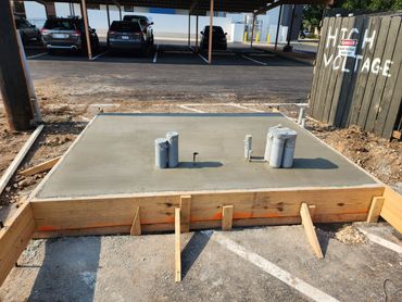Freshly poured concrete slab with pipes, next to a high voltage warning sign.