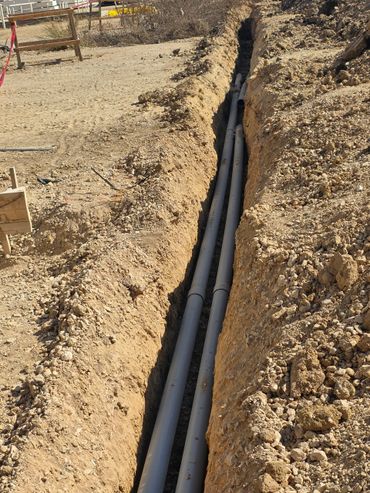 Two long gray pipes laid in a narrow trench at a construction site.