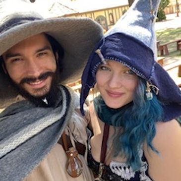 Two people in medieval fantasy costumes smiling outdoors.