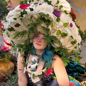 Person with blue hair wearing a large floral hat and costume.