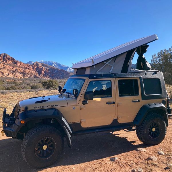 A 4-door 4x4 Jeep Rubicon with pop-up camper top conversion parked off-road in the desert near Moab,