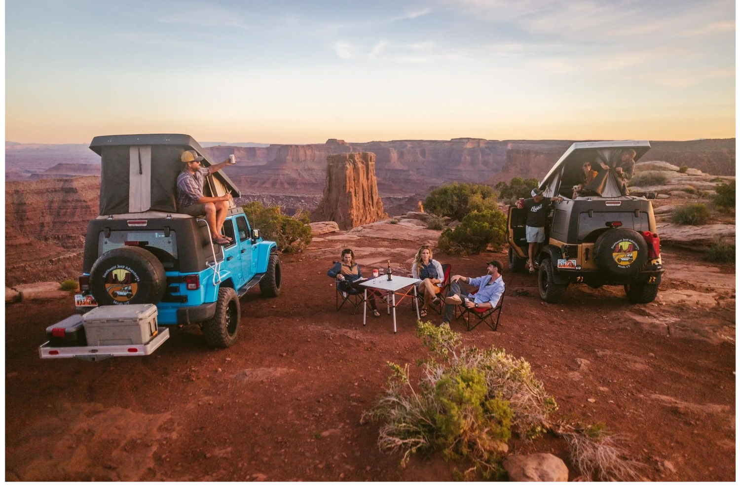 Two families camping with pop-top Jeep vehicles near the rim of a redrock canyon in Moab, Utah