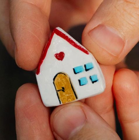 A small ceramic house held between fingers.