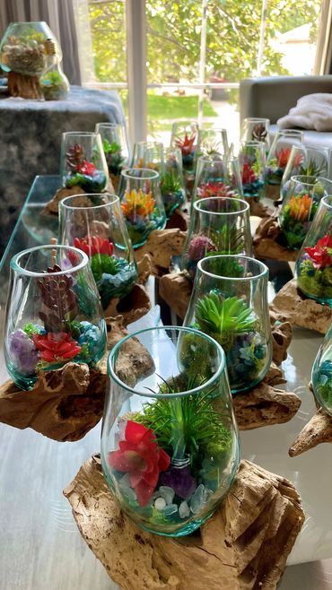 handcrafted glass planters featuring vibrant faux succulents, gemstones, and moss on driftwood bases.