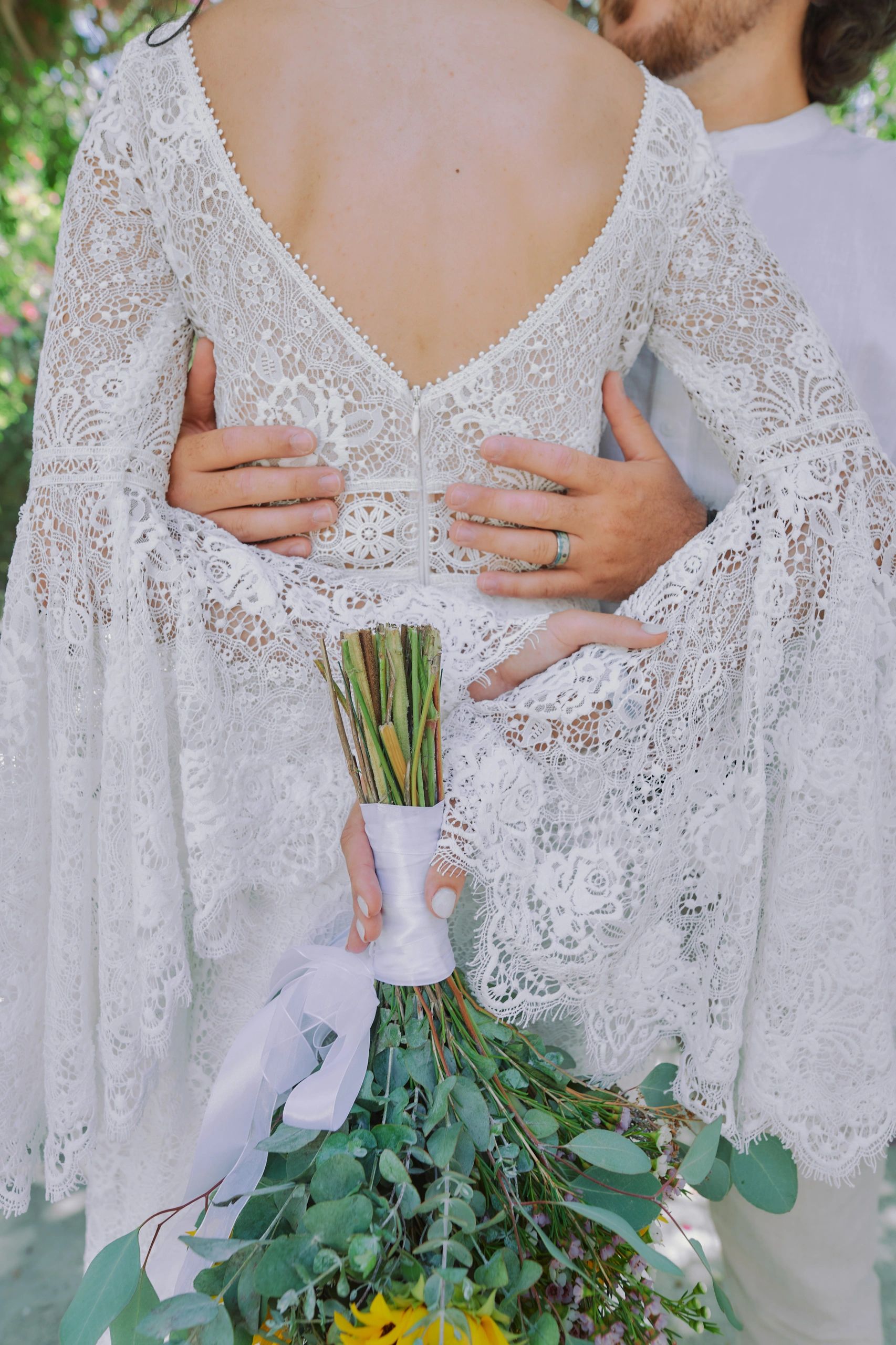Bride in a lace dress holding a bouquet, embraced by groom.