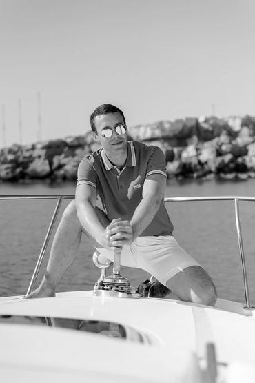 Man in sunglasses relaxing on a boat near rocky shore.