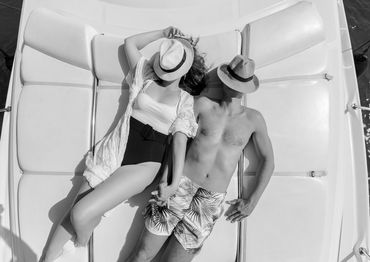 Couple relaxing on a boat, wearing hats and holding hands.