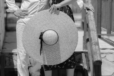 A couple stands on steps with a large straw hat in front.