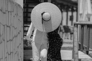 Couple embracing on outdoor steps, woman wearing large straw hat.