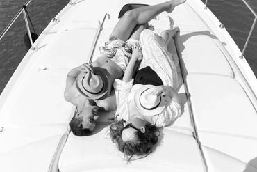 Couple relaxing on a boat, each holding a hat and enjoying the sun.