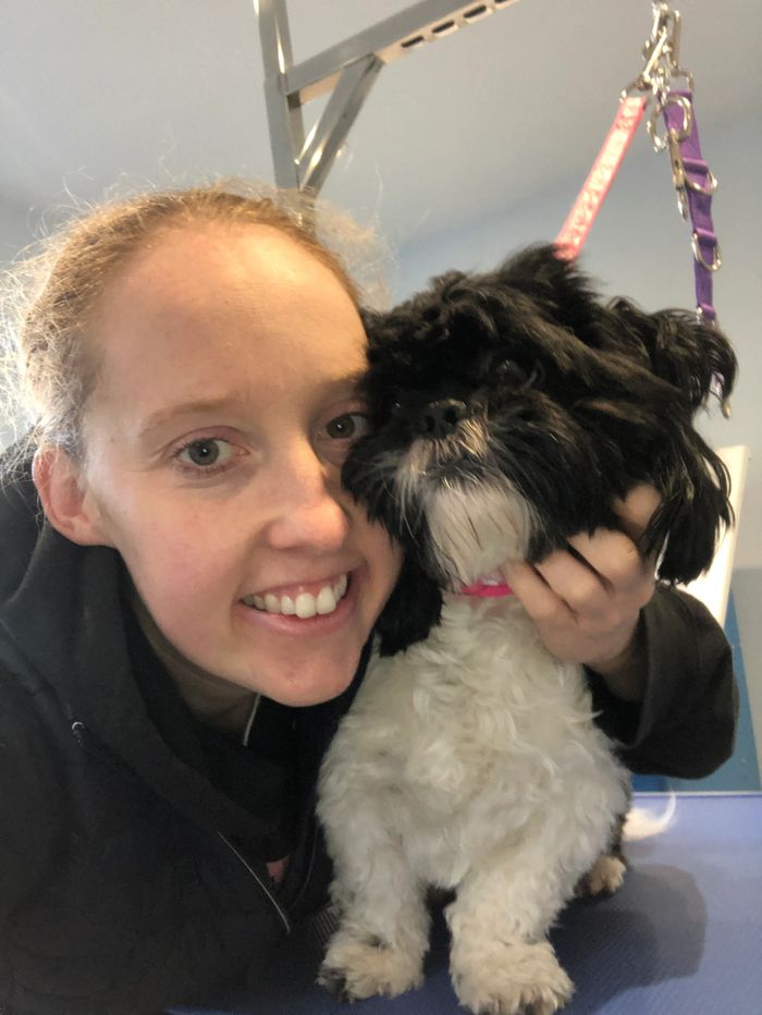 Smiling person cuddling a small black and white dog indoors.