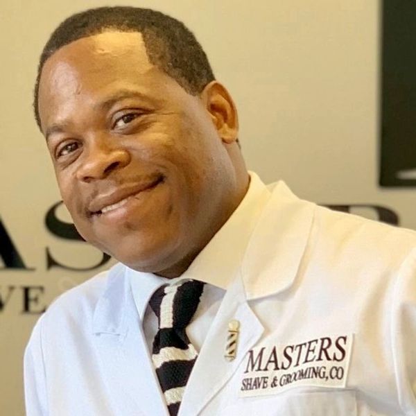 Smiling man in a white coat with Masters Shave & Grooming logo.