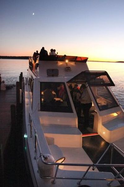 People enjoying a boat ride at sunset with a crescent moon overhead.