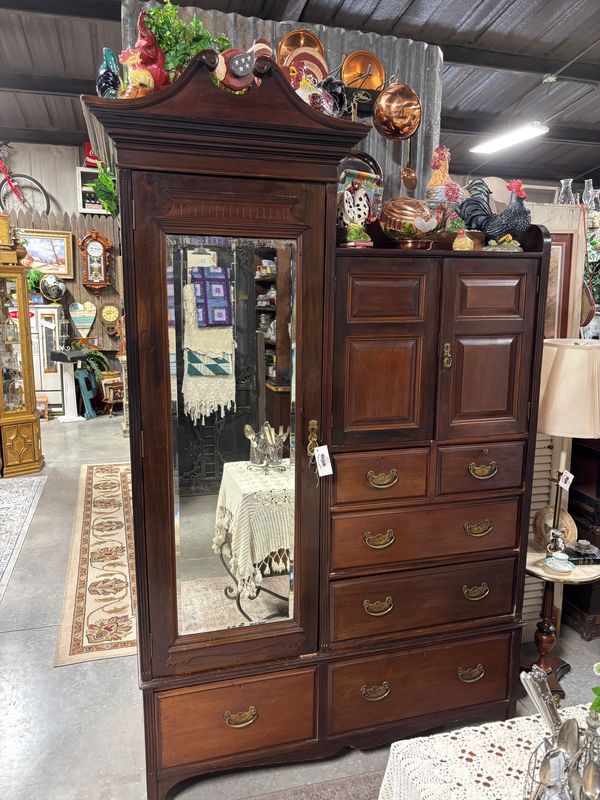 Tall antique wooden armoire with mirror and decorative rooster figurines on top.