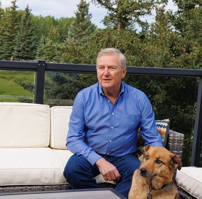A man in a blue shirt sits on a patio sofa with his dog at his feet.