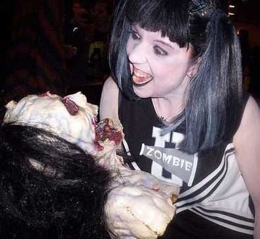 Person with zombie makeup holding a zombie prop in a dark setting.