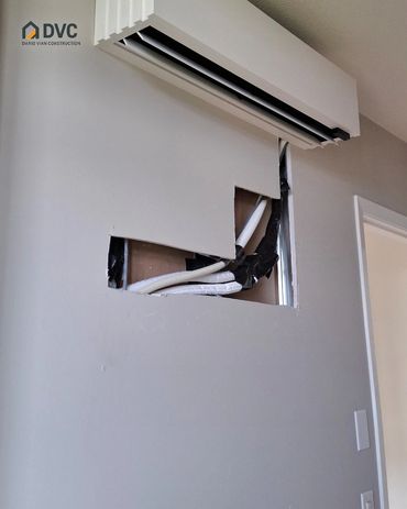 Open wall section beneath a wall-mounted unit with exposed lines before drywall repair