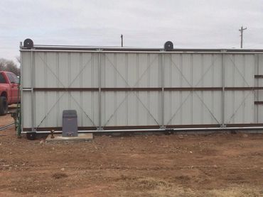 A large metal sliding gate on a dirt ground with a red pickup truck partially visible.