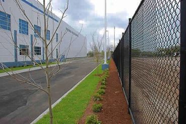 Chain-link fence separating an industrial building from an empty lot on a cloudy day.