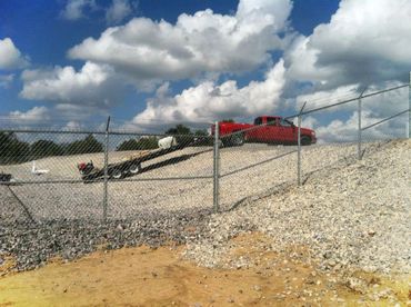 Red pickup truck parked on a gravel hill behind a chain-link fence.
