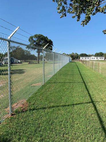 Long chain-link fence with barbed wire on top under clear blue sky.