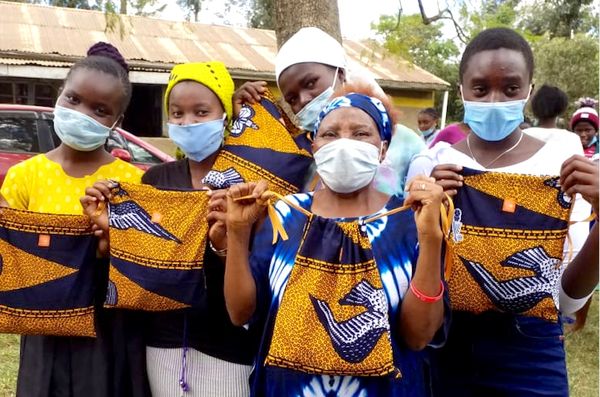 Group of women wearing masks holding handmade fabric bags outdoors.