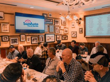 Group of people gathered in a cozy restaurant with SunAuto Tire & Service displayed on a screen.